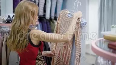 来访者的女人拿了两个带连衣裙的衣架搬到服装店的试衣间，因为她在身上试衣